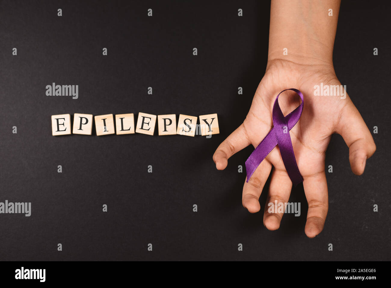 Purple ribbon on cramps hand and EPILEPSY word against black background. Concept of epilepsy awareness Stock Photo