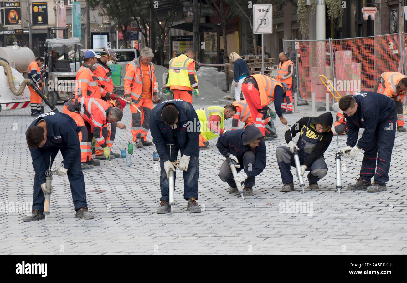 Belgrade, Serbia -  October 17, 2019: Group of construction workers in blue and city sanitation workers in orange using caulking guns and tiny paintbr Stock Photo