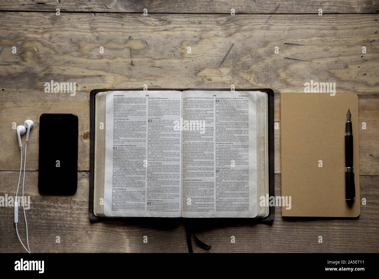 Overhead shot of opened bible in the middle of a notebook and a smartphone on a wooden surface Stock Photo