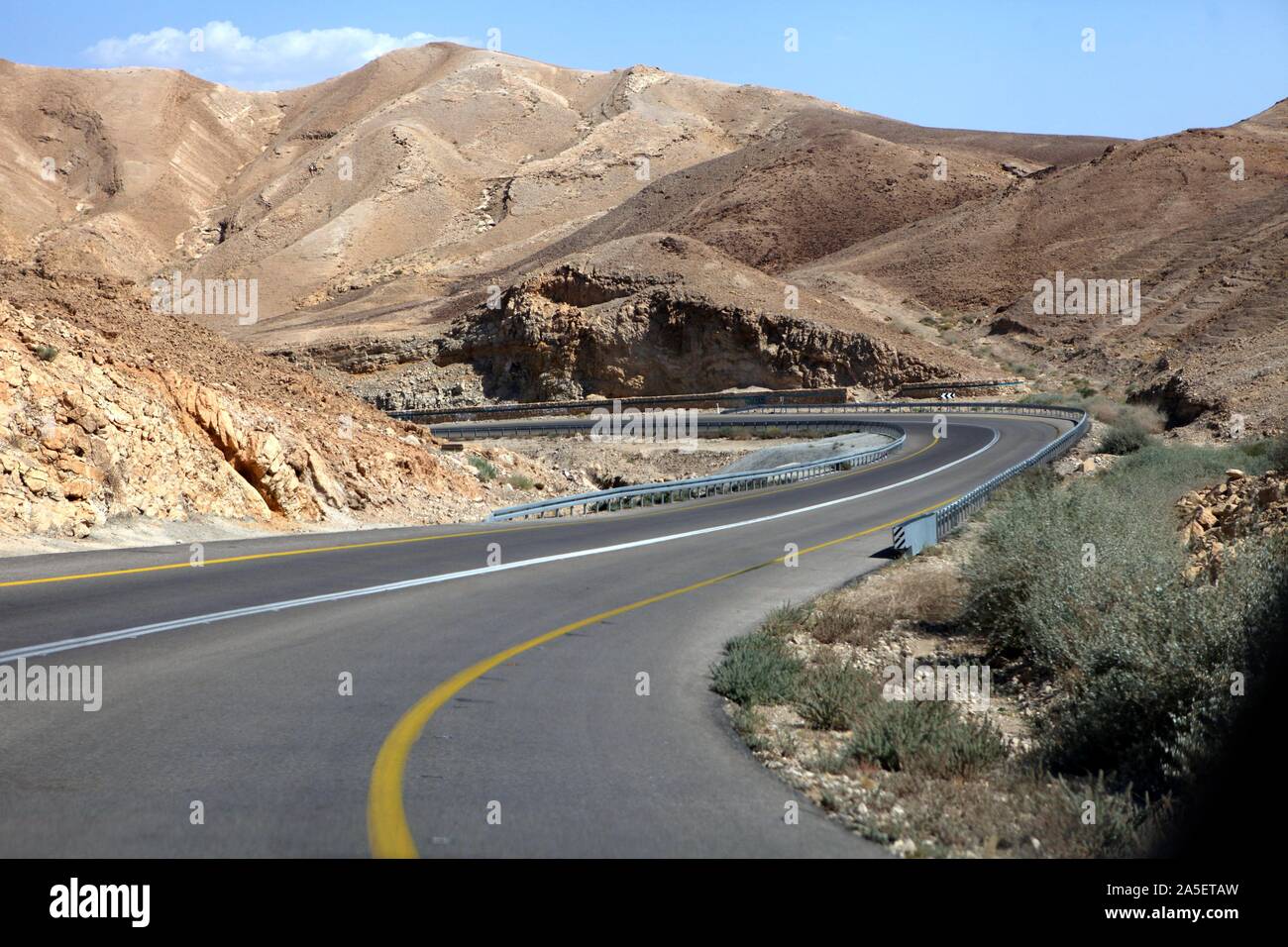 curvy sandy road on a highway that runs along the Dead Sea from one side and Edom Mountains at Arava Desert from the other in Israel. Stock Photo
