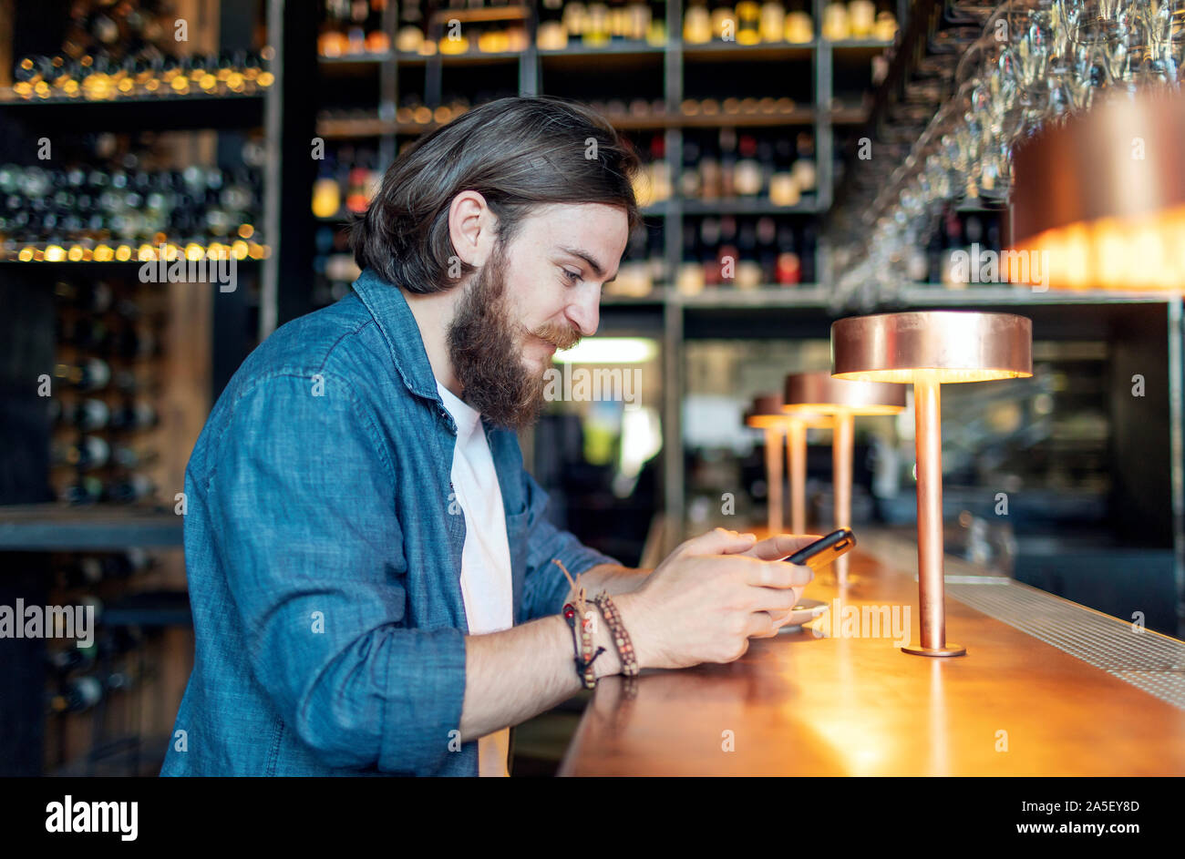 Young brown-haired bearded man using smartphone by a bar Stock Photo