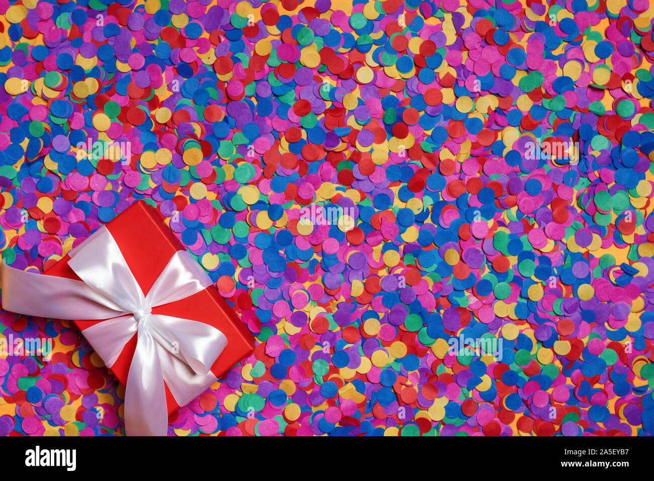 Red box with a gift on scattered confetti. Top view. Stock Photo