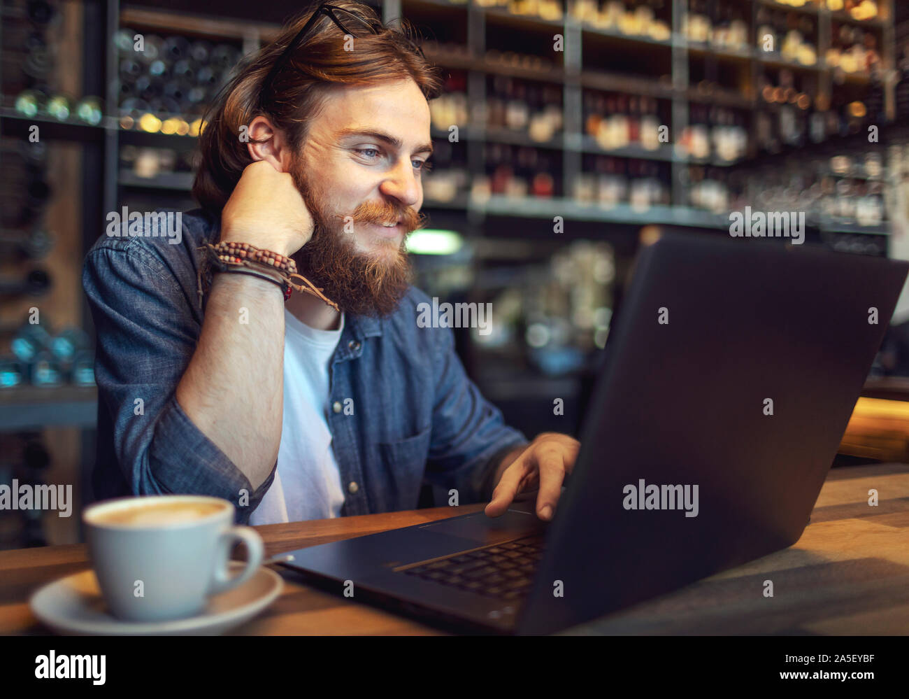 Contented smiling bearded lad working by laptop in a bar Stock Photo
