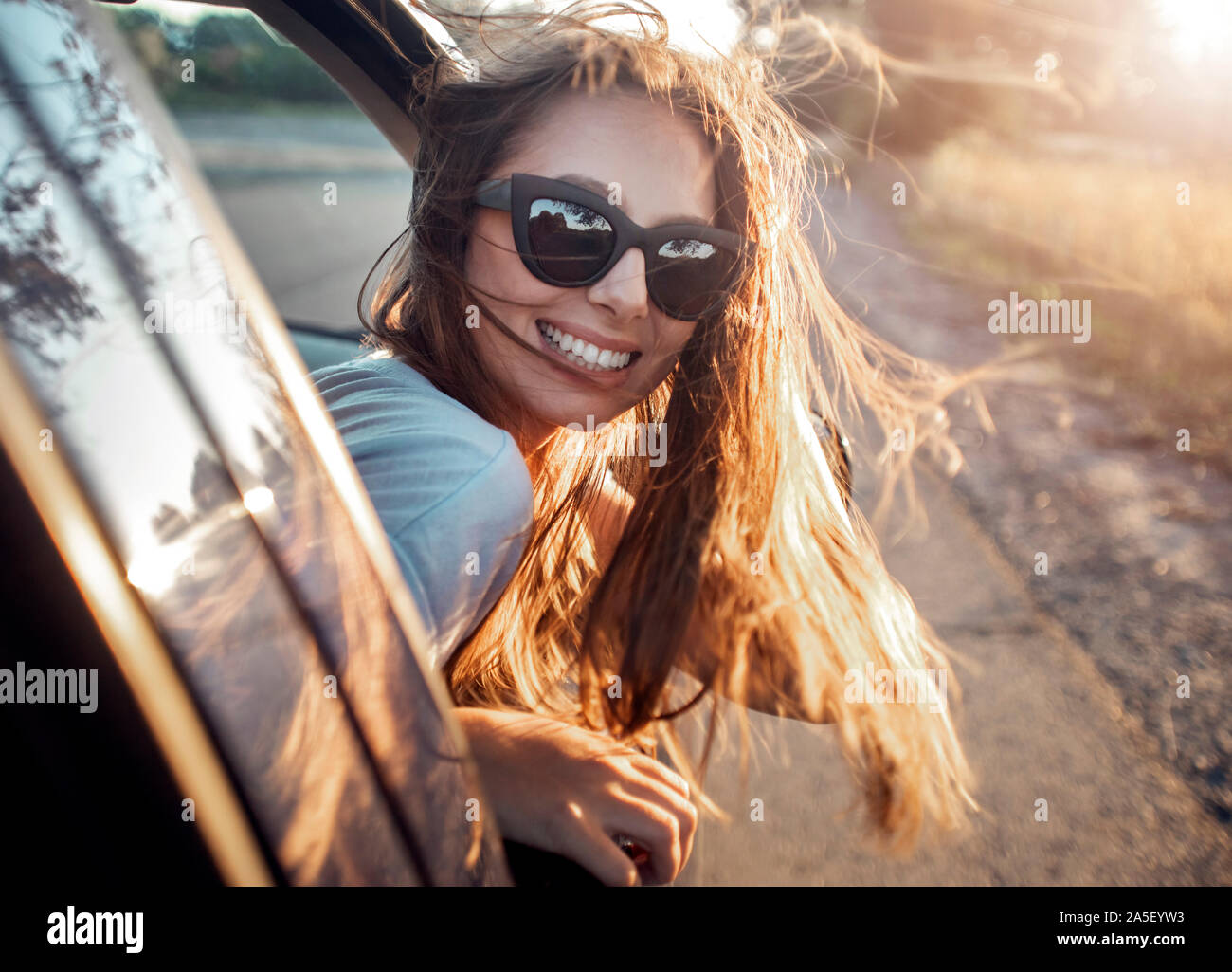Cute brunette with long fluttering hair leaning out of the window of a car Stock Photo