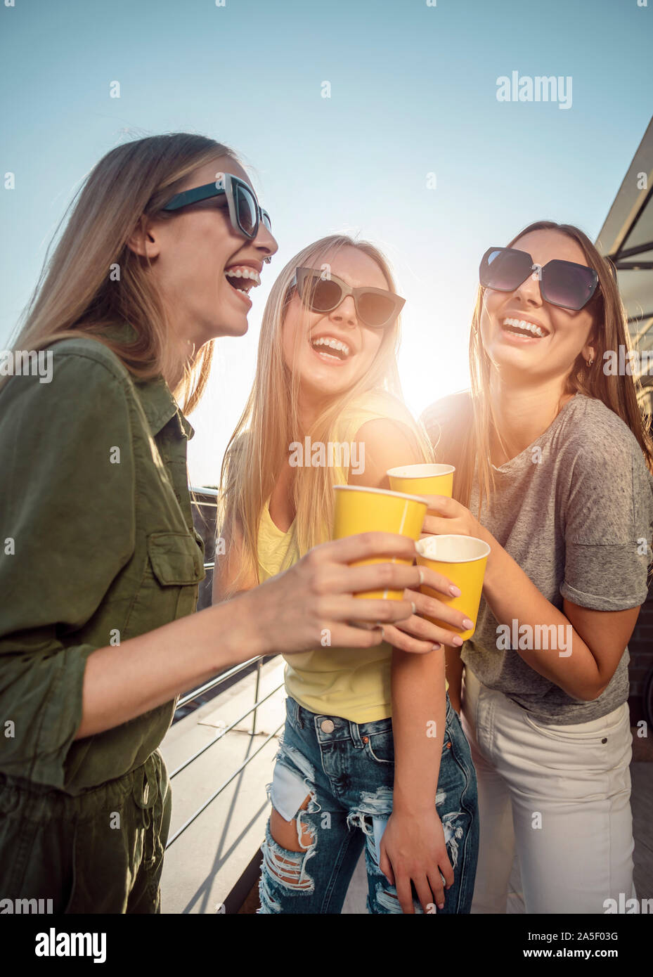 Smiling pretty women in sunglasses drinking on a sunny balcony Stock Photo