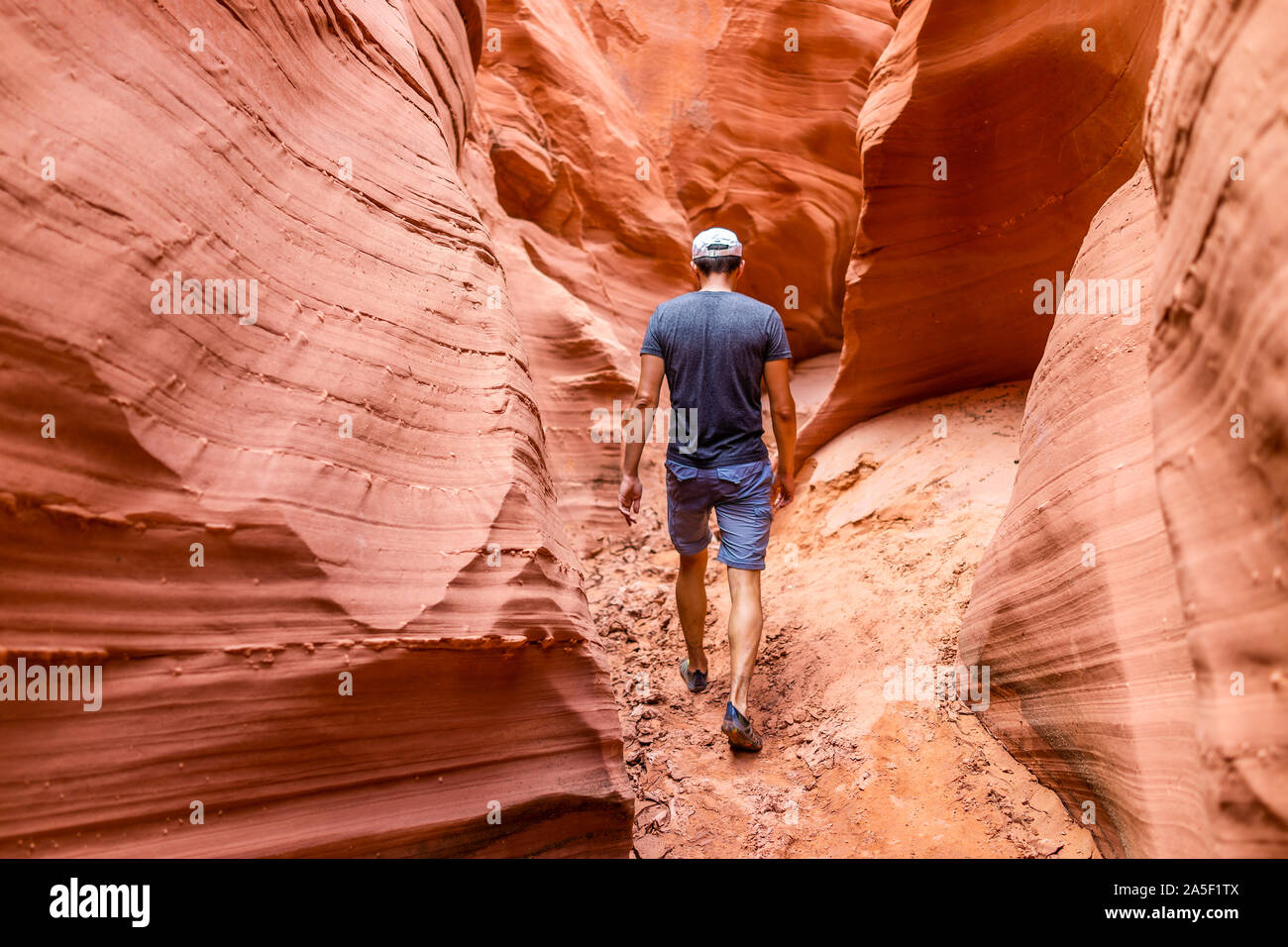 Orange red wave shape formations rocks shadows with back of man walking at narrow Antelope slot canyon in Arizona on footpath trail from Lake Powell Stock Photo