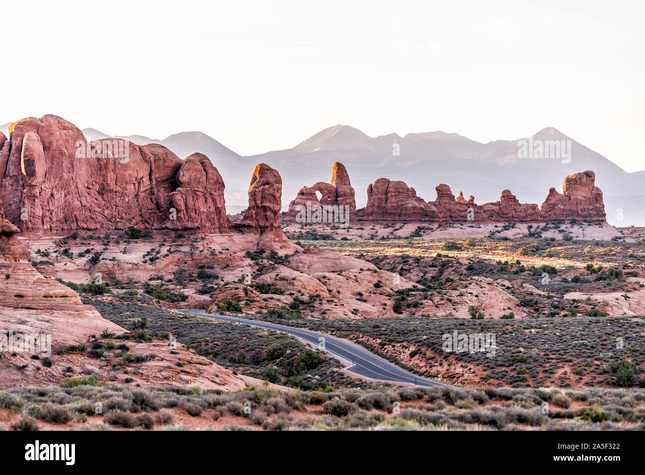 High angle view of empty road leading to window arch in Arches National Park in Utah during morning sunrise with orange red pink rock color Stock Photo