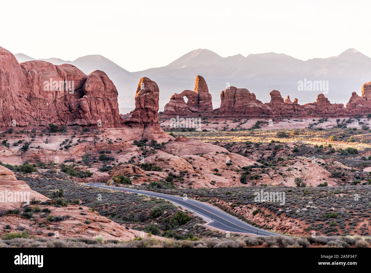 High angle aerial view of road leading to window arch in Arches National Park in Utah during morning sunrise with orange red pink rock color Stock Photo