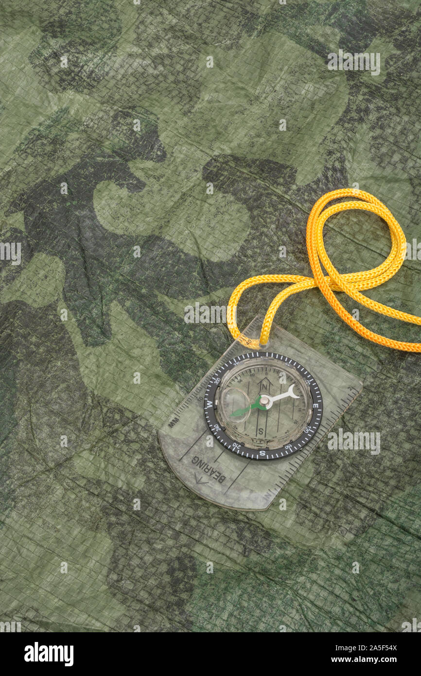 Section of worn camouflage ground sheet / groundsheet material and small pocket compass with yellow lanyard. Survival gear concept, emergency gear. Stock Photo