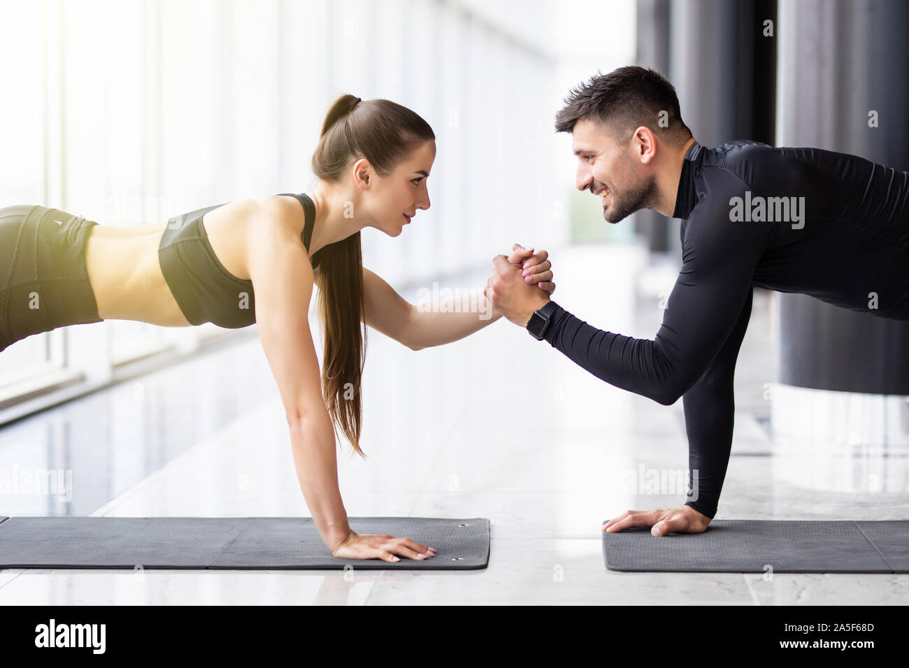 Slim girl and strong man are standing in one hand plank position and balancing on that hand. They look concentrated and concious. Stock Photo