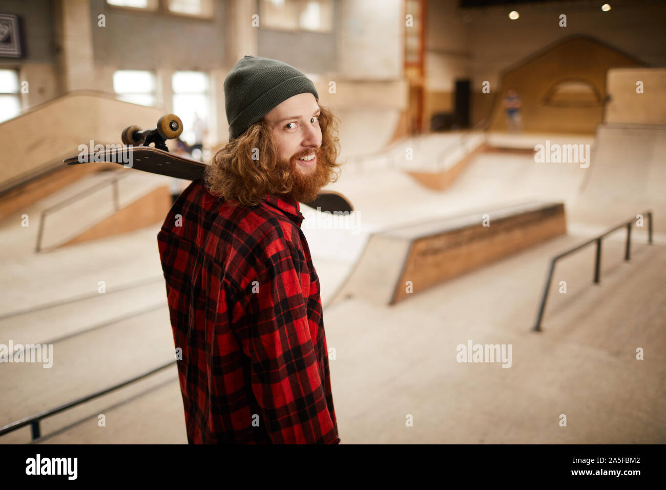 Waist up portrait of hipster man looking at camera over shoulder while posing in skating park, copy space Stock Photo