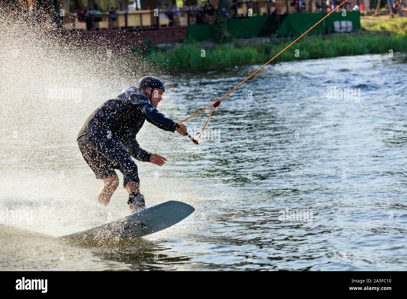Wakeboarder rushes through the water along the grassy banks of the ...