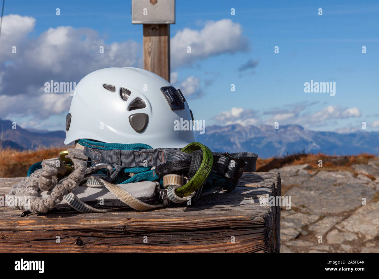 Climbing safety gear lying on a table on a mountain summit. A helmet and climbing harness are shown in front of a summit cross. In the background a mo Stock Photo