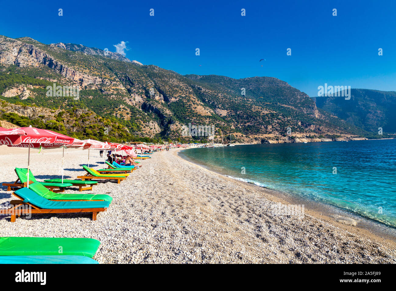 Shingle beach and sun loungers with parasols in Oludeniz, Turkish Riviera, Turkey Stock Photo