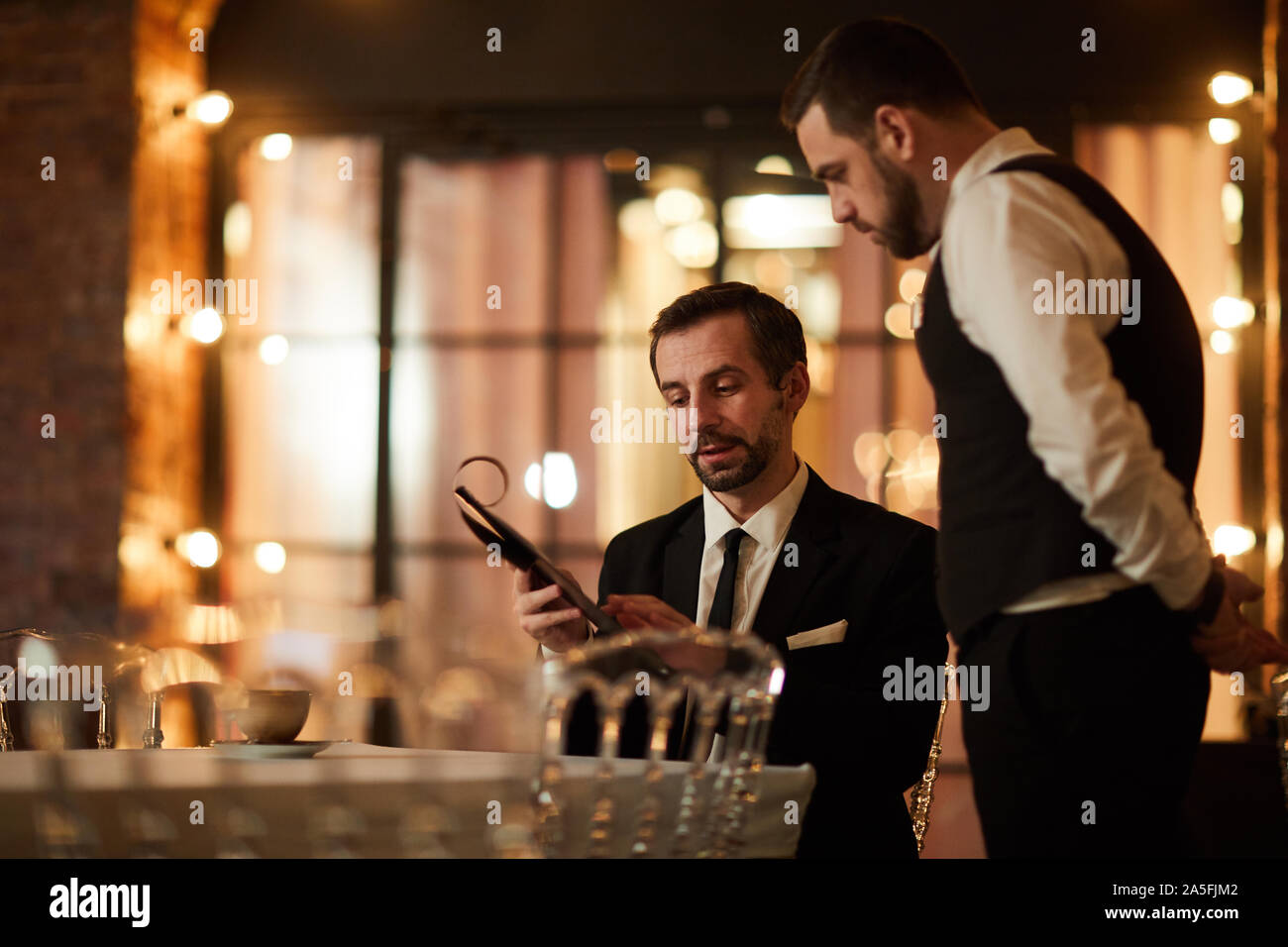 Portrait of mature bearded businessman looking at menu while ordering dinner in luxury restaurant, copy space Stock Photo