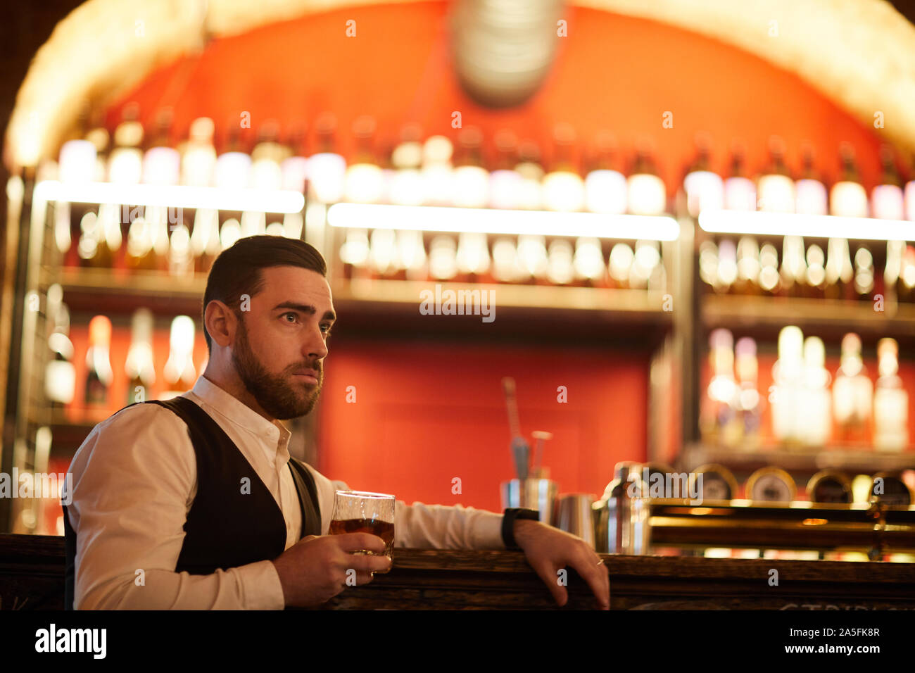 Side view portrait of pensive bearded businessman drinking whiskey sitting by bar counter and relaxing after work, copy space Stock Photo