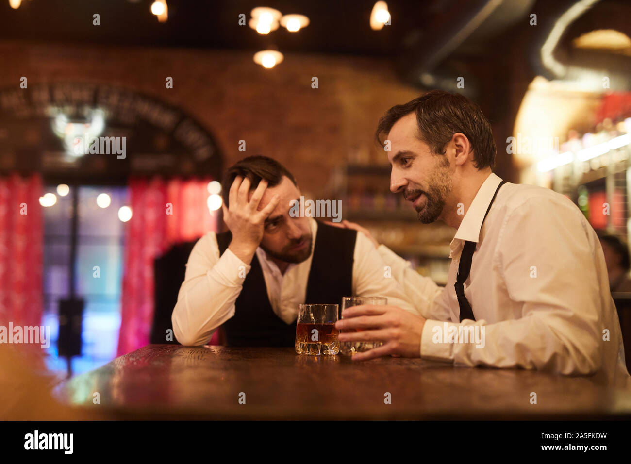 Portrait of two drunk business people talking sitting at table in bar