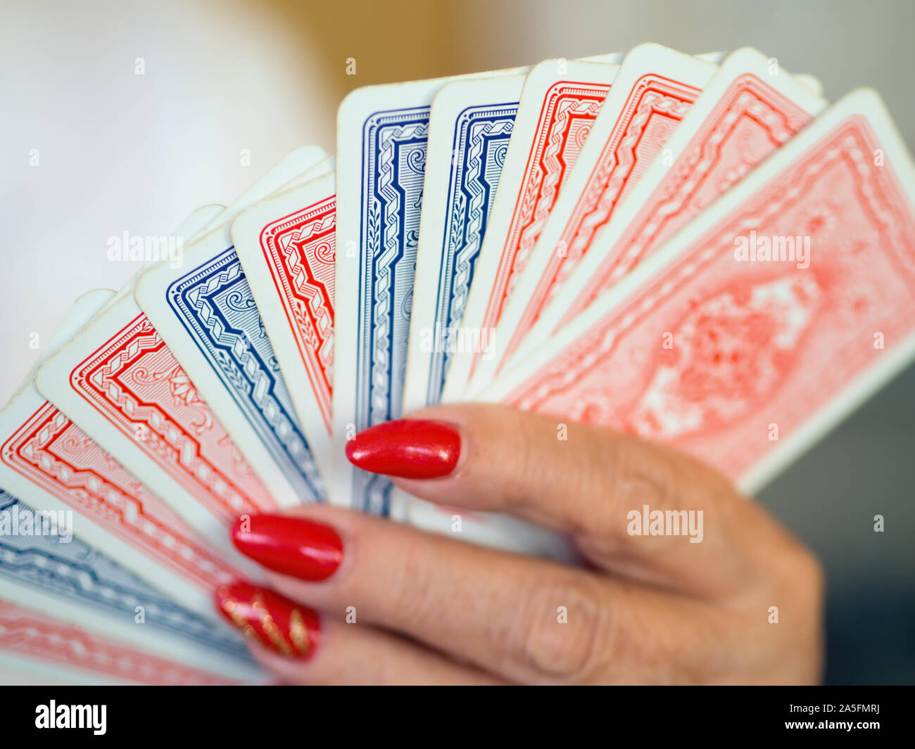 Playing cards in blue and red design with the back lined up in a female hand with red lacquered nails. Focus on Point, the rest light Bookeh. Close-up Stock Photo