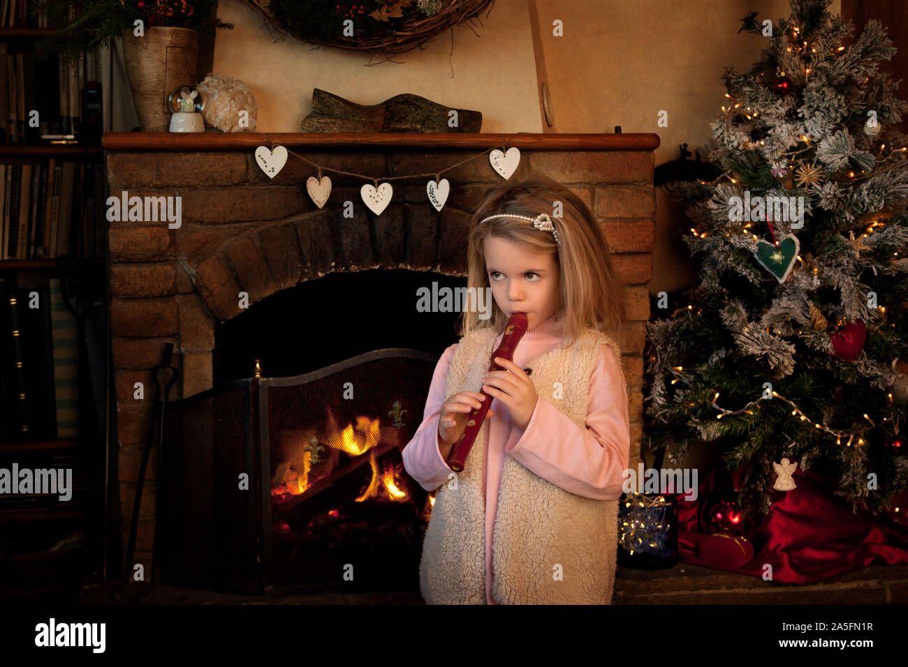 Girl standing in front of a fireplace at Christmas playing the recorder Stock Photo