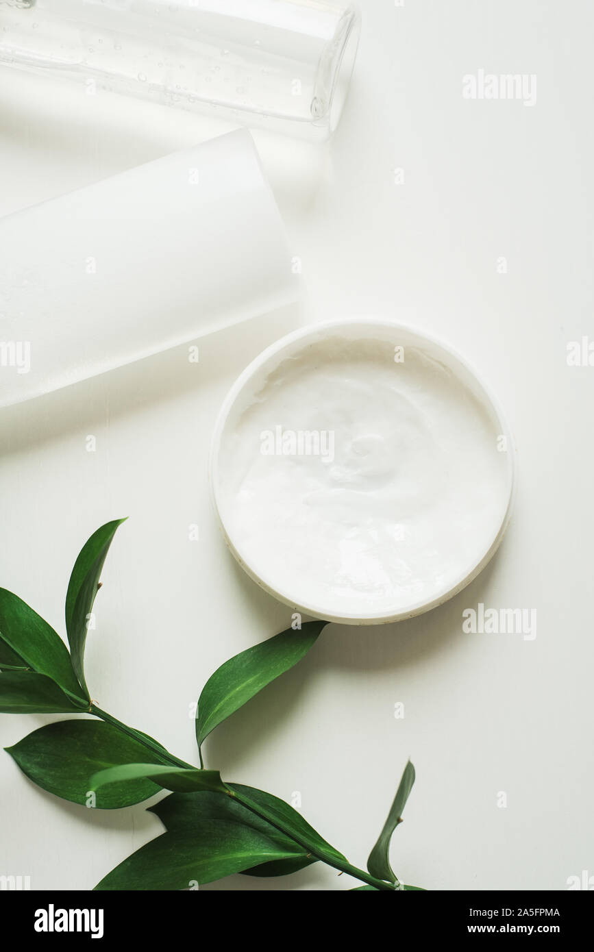 Means for skin care, rejuvenation and hydration of the face. Cream, micellar water and moisturizing lotion on a white background with a branch of green . The philosophy of self care and skin care. Stock Photo