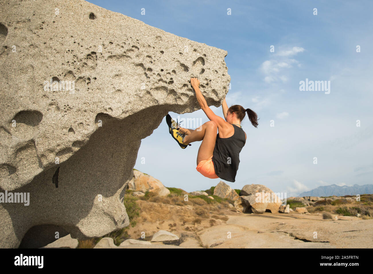 Woman rock climbing on natural boulder rock at the beach, Corsica, France Stock Photo