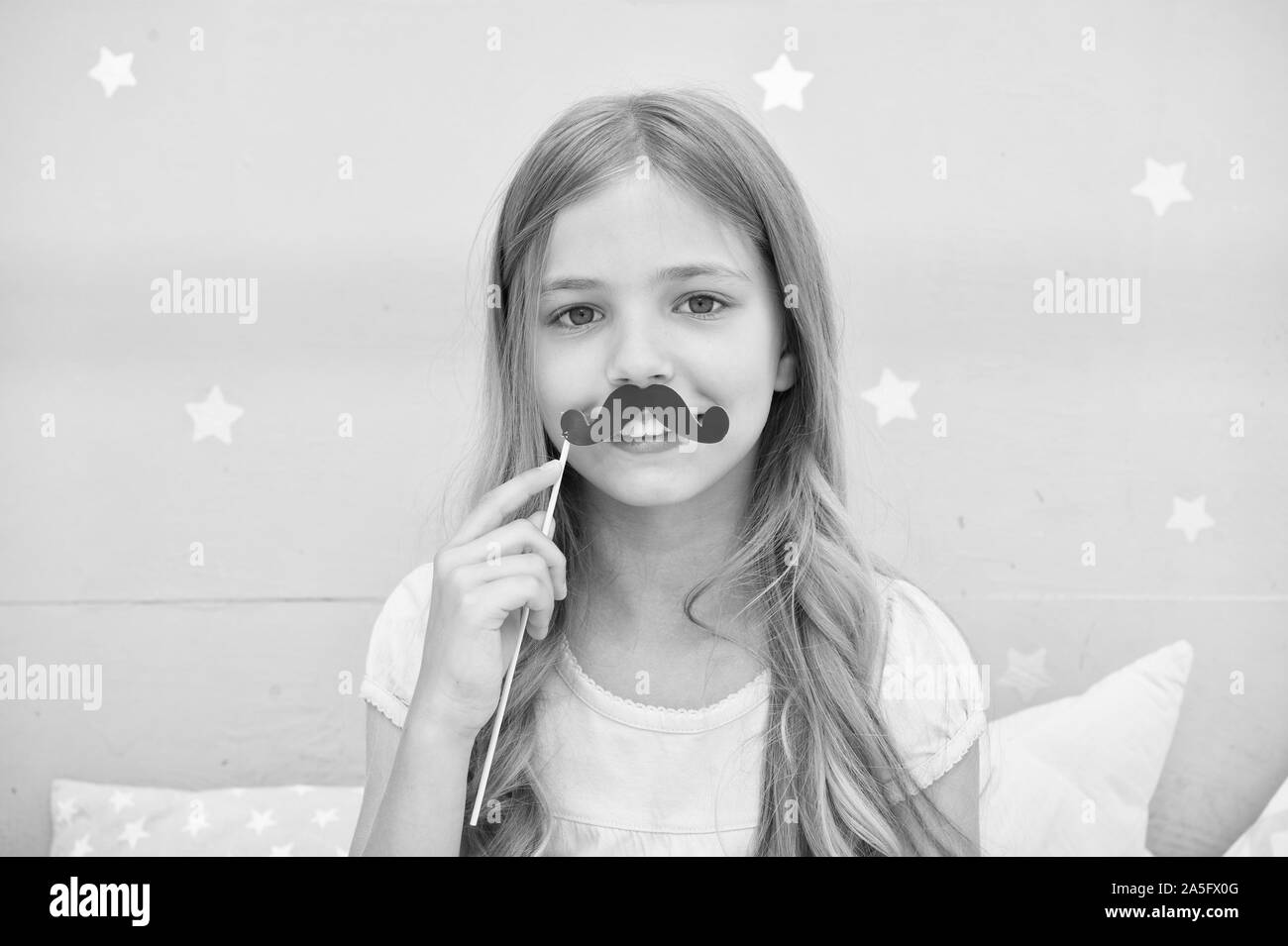 Having fun with fake mustache. Happiness and humor concept. Kid long hair happy smile face. Girl carefree child having fun with mustache. Play with mustache photo booth props. Hair care and beauty. Stock Photo