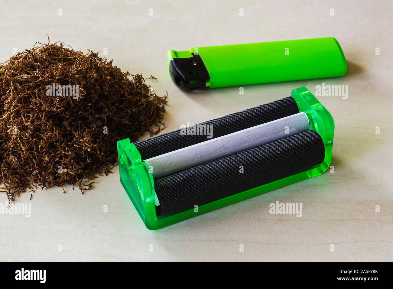 can you make cigarettes with pipe tobacco Green cigarette rolling machine, green lighter and pile of tobacco on a  white table. Making cigarettes with pipe tobacco at home. Front view Stock  Photo