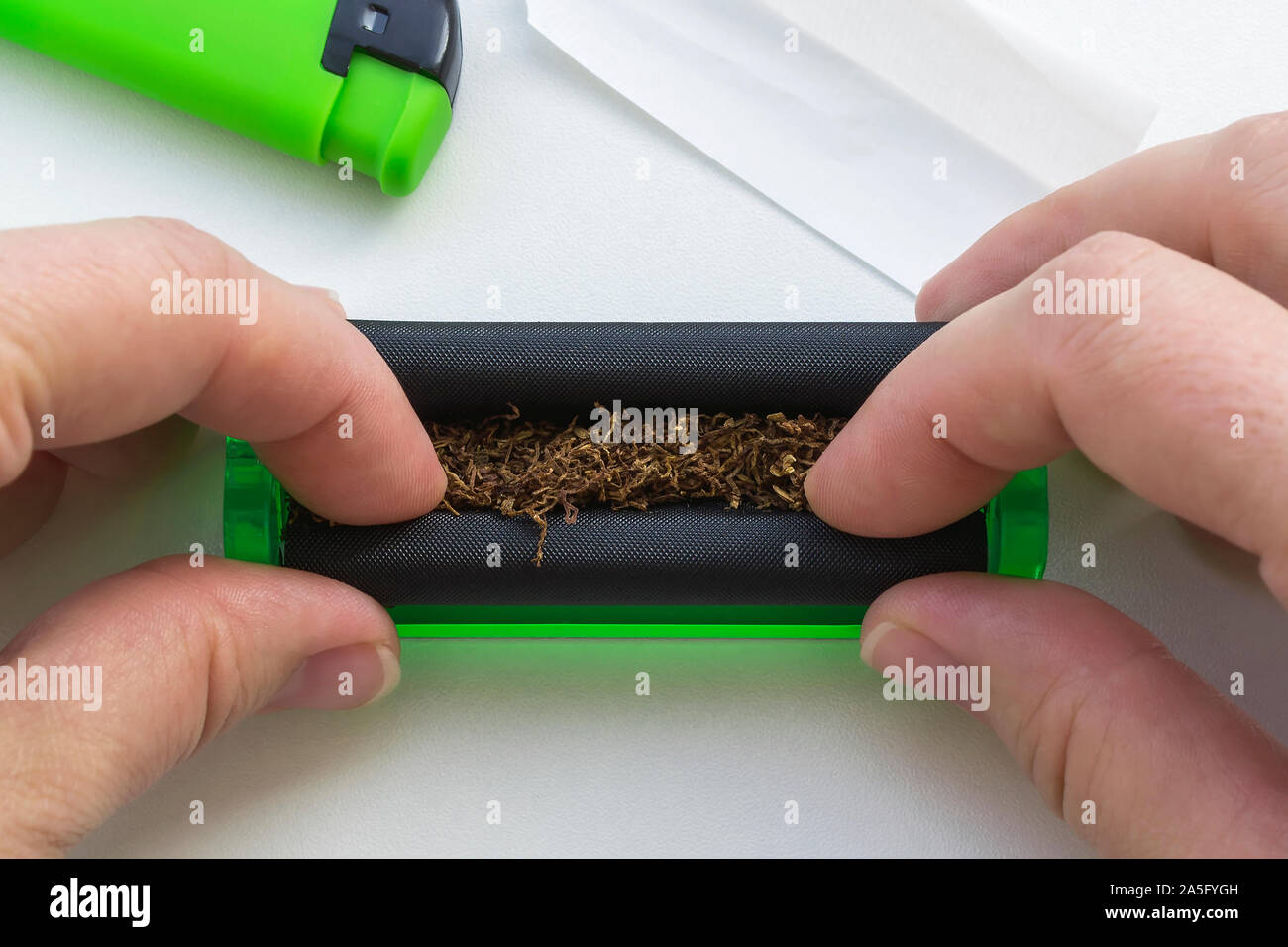 Woman hands making a cigarette with green rolling machine near green lighter and cigarette paper