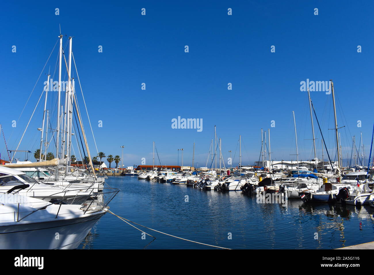 Sailboats on water pictured on a sunny day in the French Riviera. Luxury yachts on the dock marina in a resort in south of France. Tall palm trees. Stock Photo