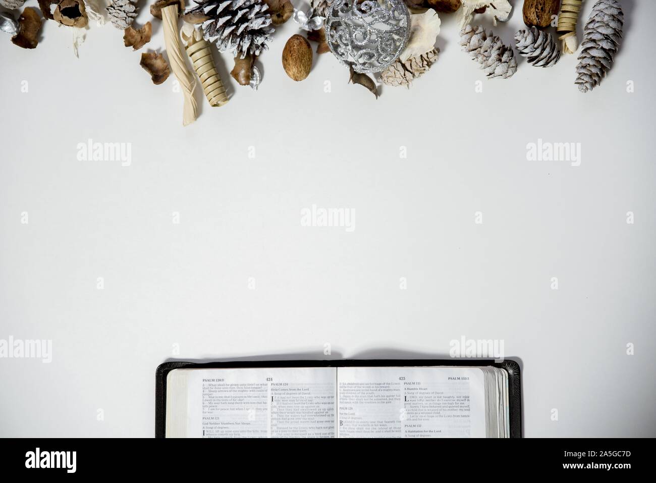 Overhead shot of an open bible on a white surface with pine cones and an ornament on the top Stock Photo