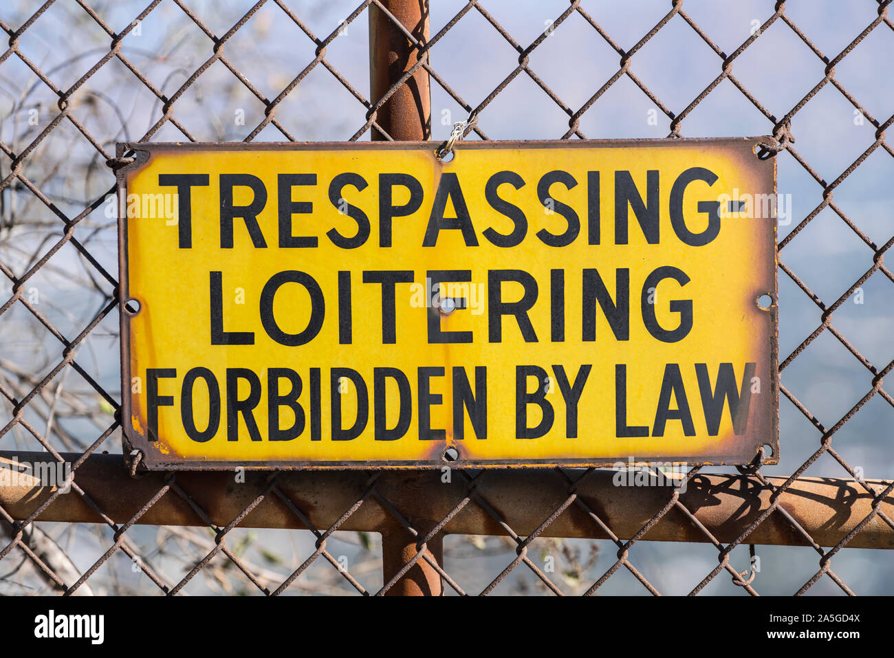 Old Trespassing and Loitering Forbidden by Law sign on rusty chain link fence. Stock Photo