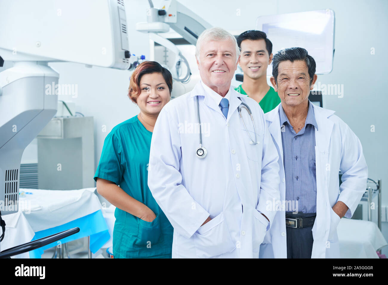 Smiling multi-ethnic group of doctors and surgeons standing in operating room of hospital Stock Photo