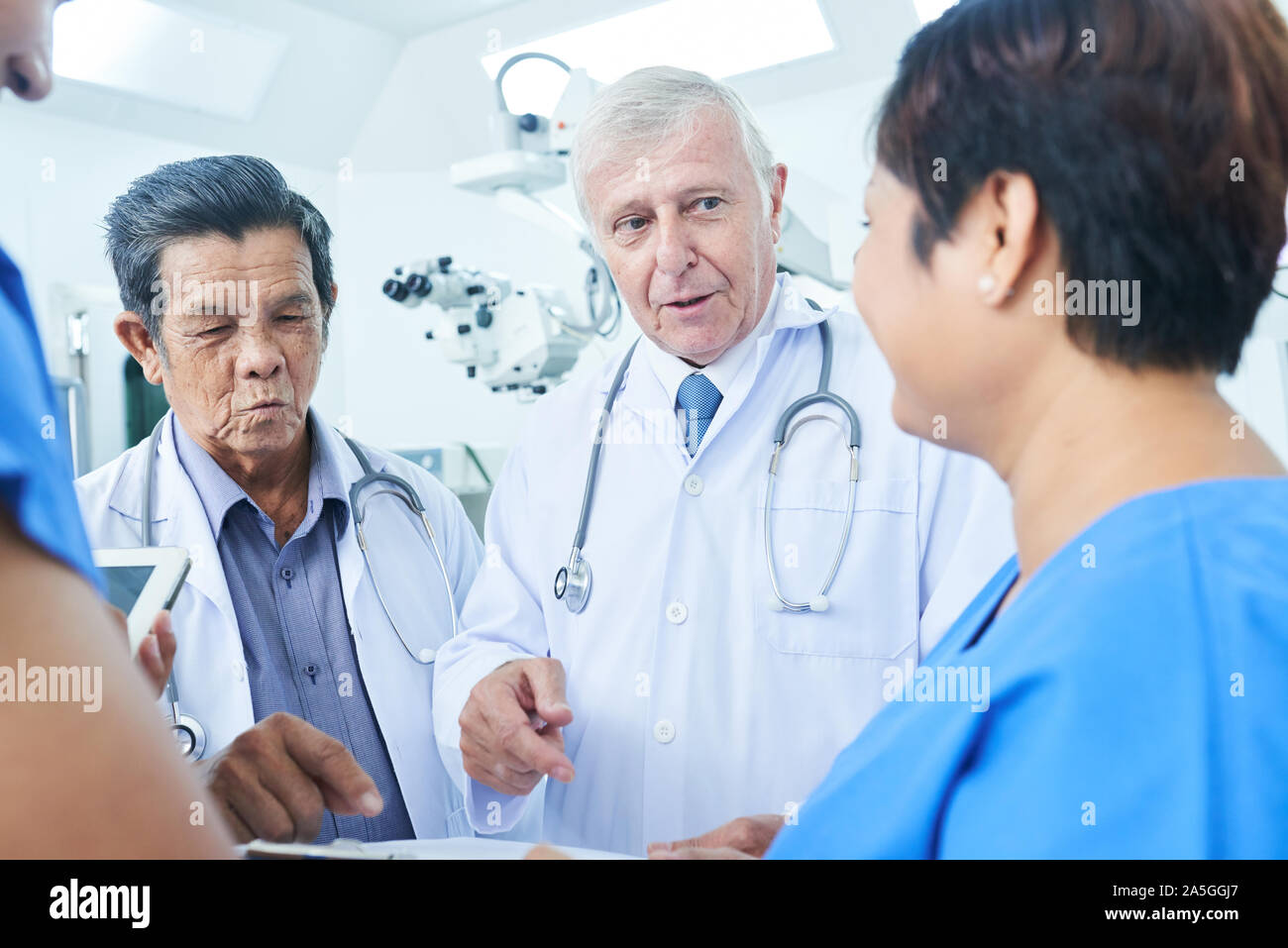 Group of doctors standing in operating room and discussing information in medical history of patient Stock Photo