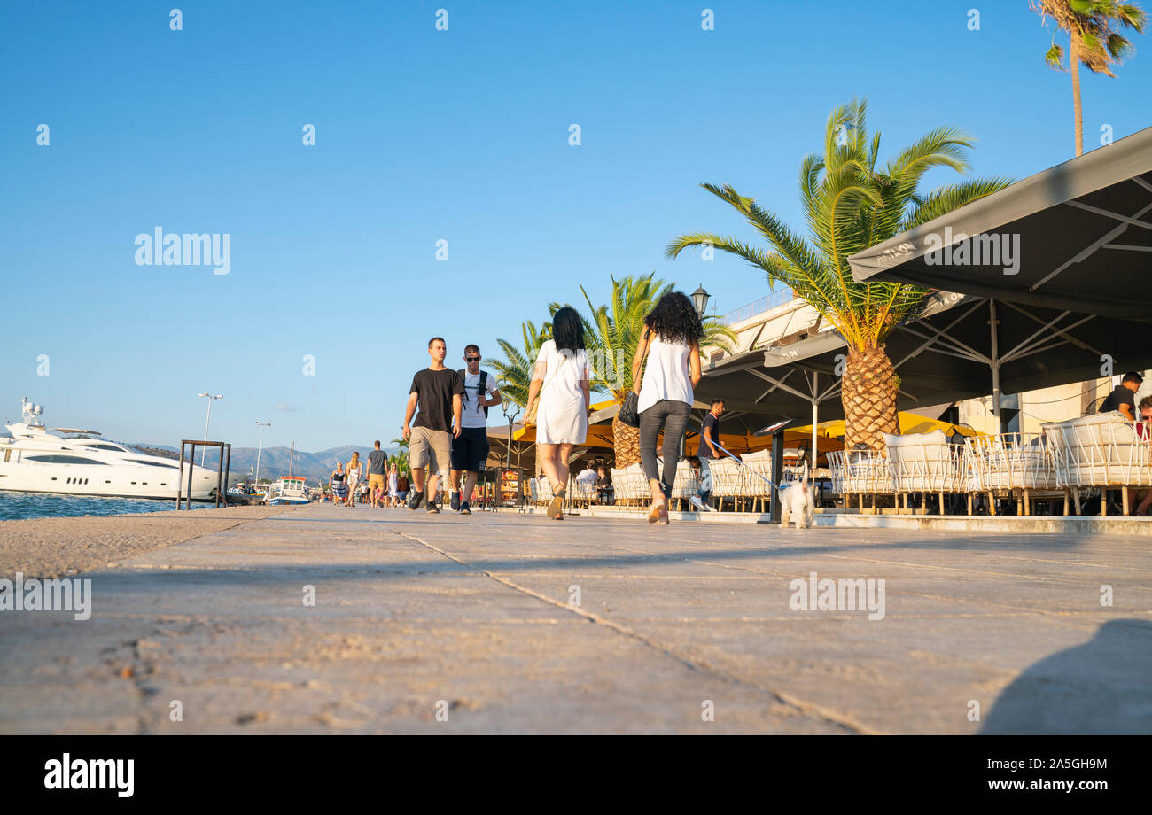 Nafplio Greece - July 17 2019; People on promenade in evening light between cafes and restaurants on one side and harbor on other. Stock Photo
