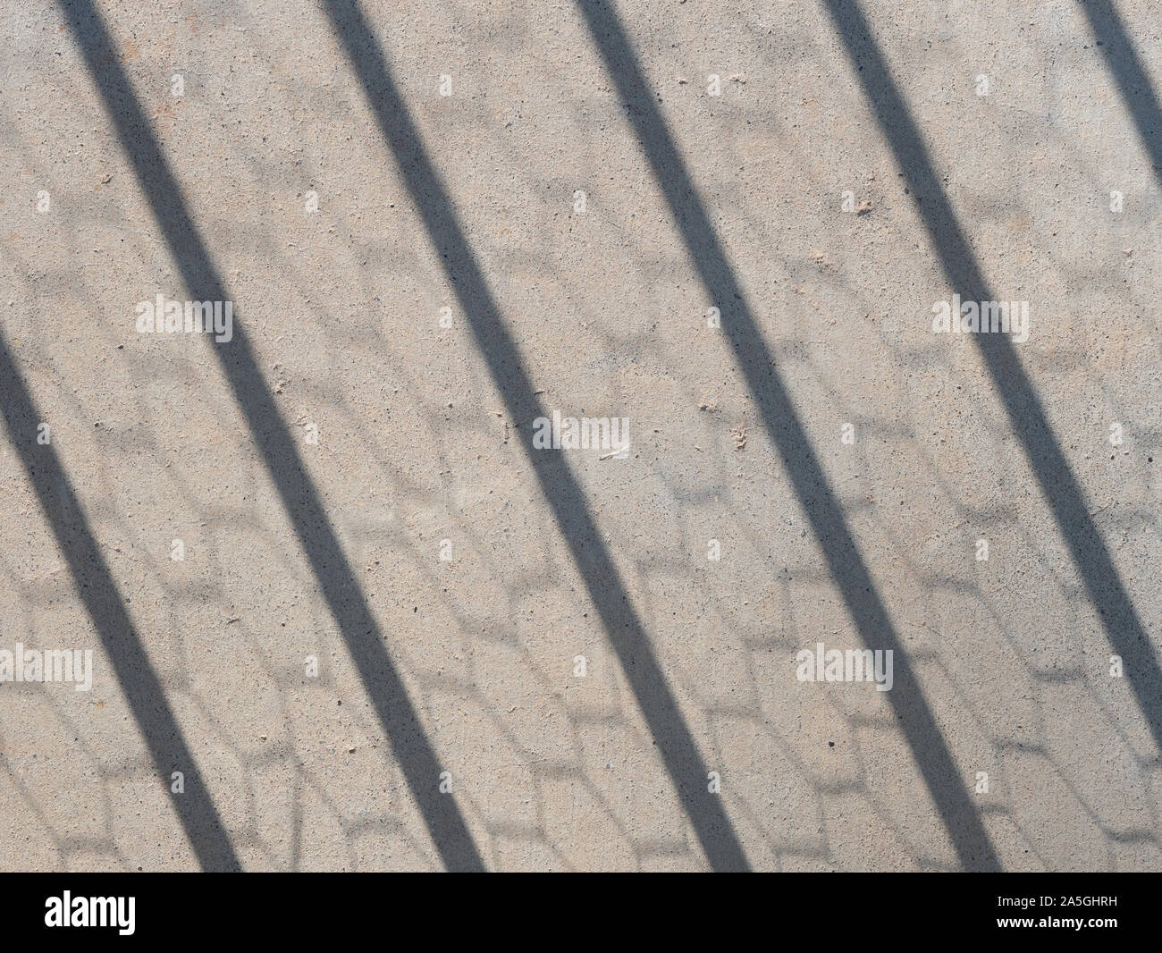 Hexagonal chicken wire and fence post shadows on a concrete sidewalk