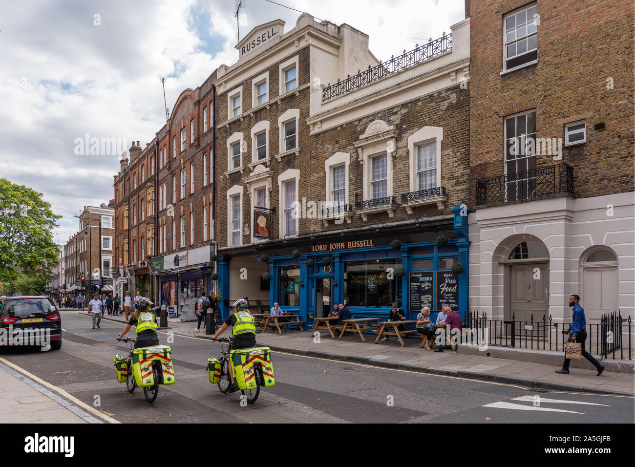 London cycle paramedics cycling down Leigh St, Saint Pancras, London. The Norfolk Arms pub in the background Stock Photo