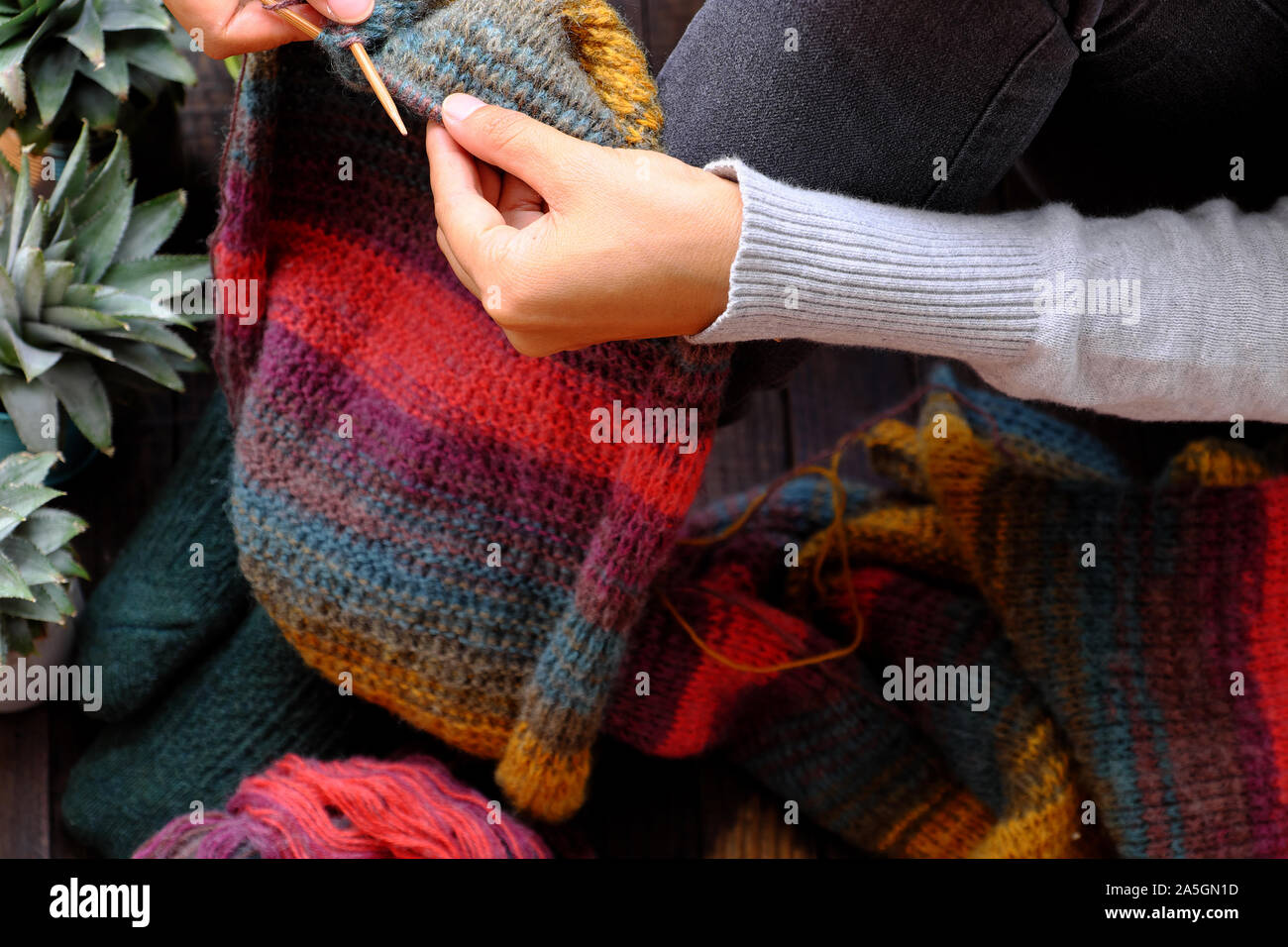 Top view woman feet with socks, sitting at home balcony, hand hold knitting needle, knit colorful wool scarf, meaningful handmade winter gift Stock Photo