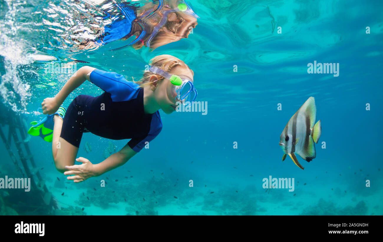 Happy family - active kid in snorkeling mask dive underwater, see tropical fish Platax (Batfish) in coral reef sea pool. Travel adventure, swimming. Stock Photo