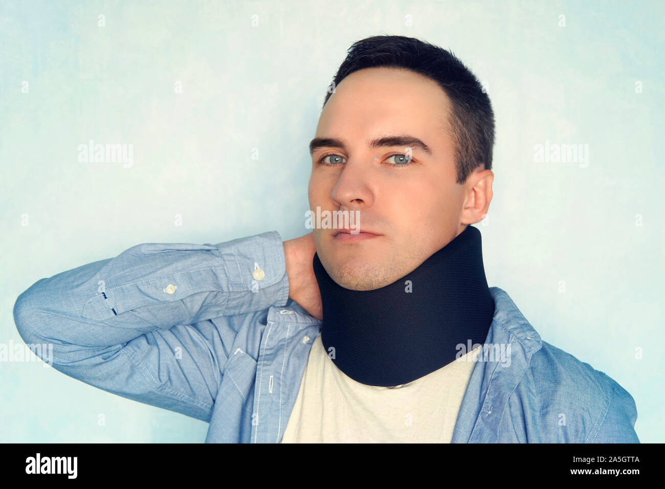 Man with neck brace after whiplash injury blue background, black neck collar on male patient. treatment of diseases of the neck and blood vessels of t Stock Photo