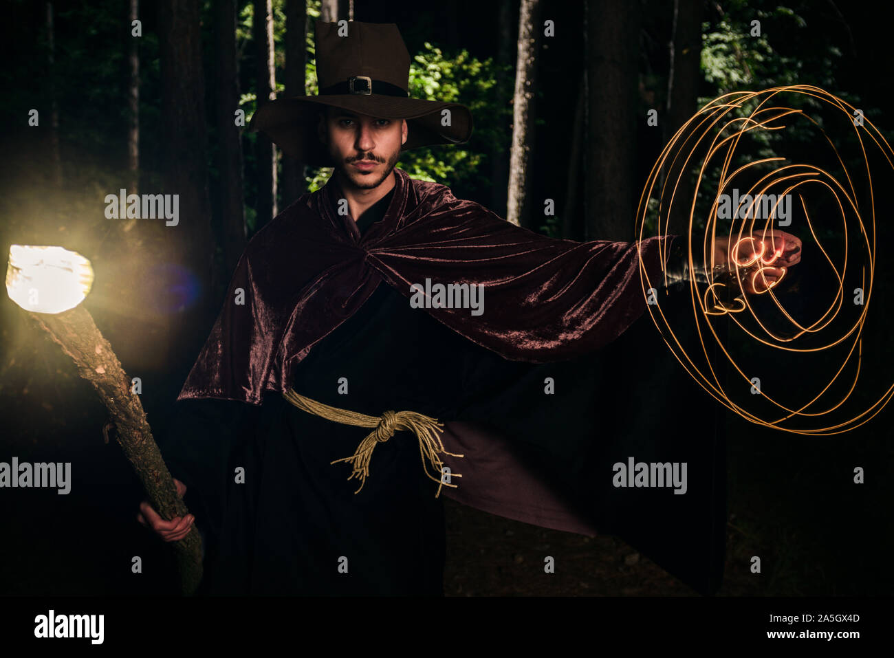 Man who is wearing wizard robes and casting glow spell with his magic staff in the woods Stock Photo