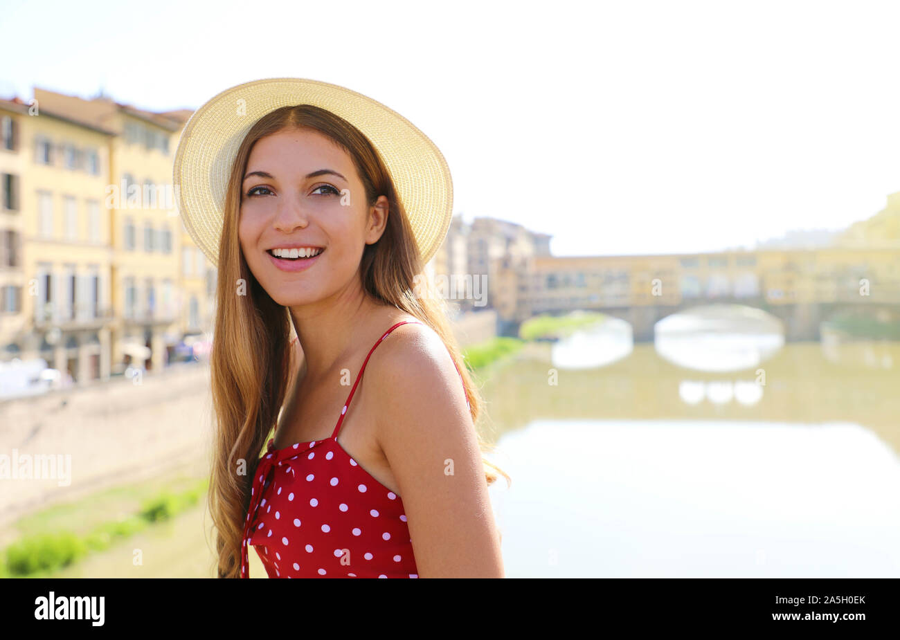 Happy smiling girl in Florence with Ponte Vecchio bridge and Arno river on the background. Portrait of young woman visiting Tuscany beauty in Italy. Stock Photo