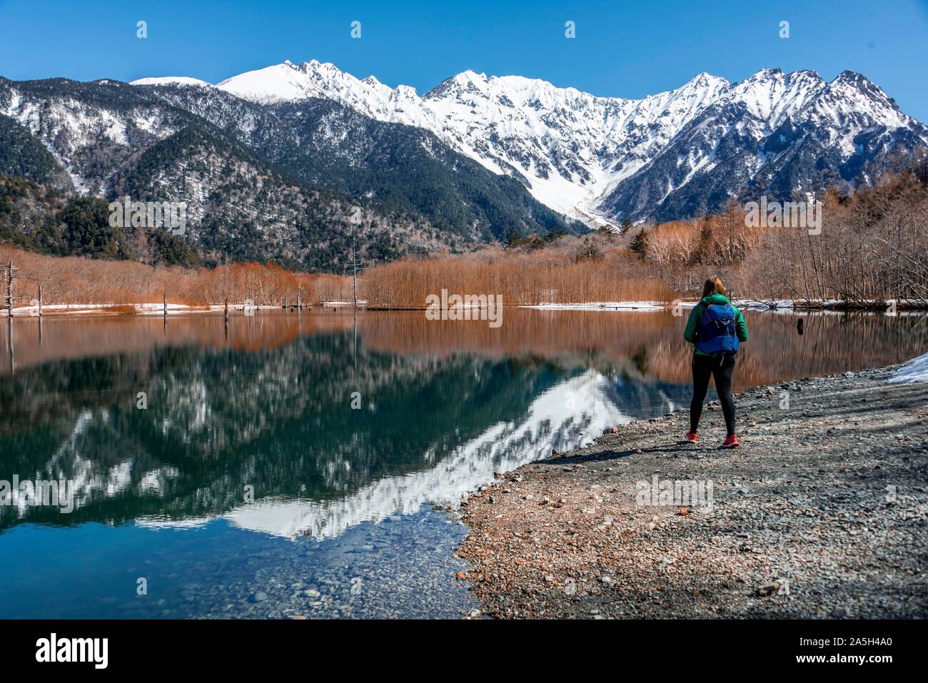 Young woman at a lake, Japanese Alps reflected in Taisho Pond, Mount Hotaka at the back, Kamikochi, Matsumoto, Nagano Stock Photo