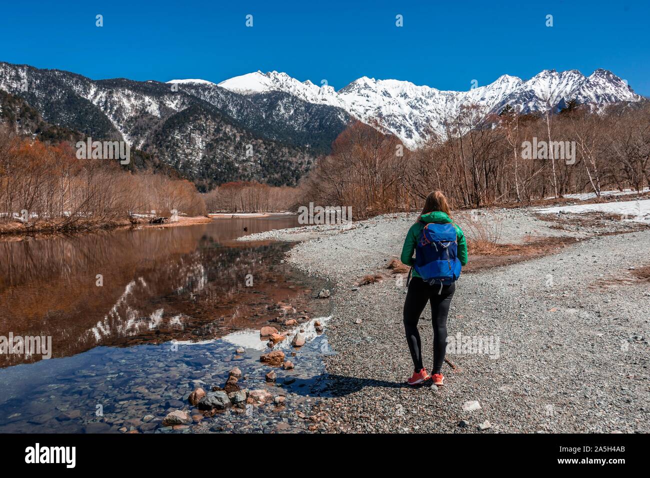 Young woman at a lake, Japanese Alps reflected in Taisho Pond, Mount Hotaka at the back, Kamikochi, Matsumoto, Nagano Stock Photo