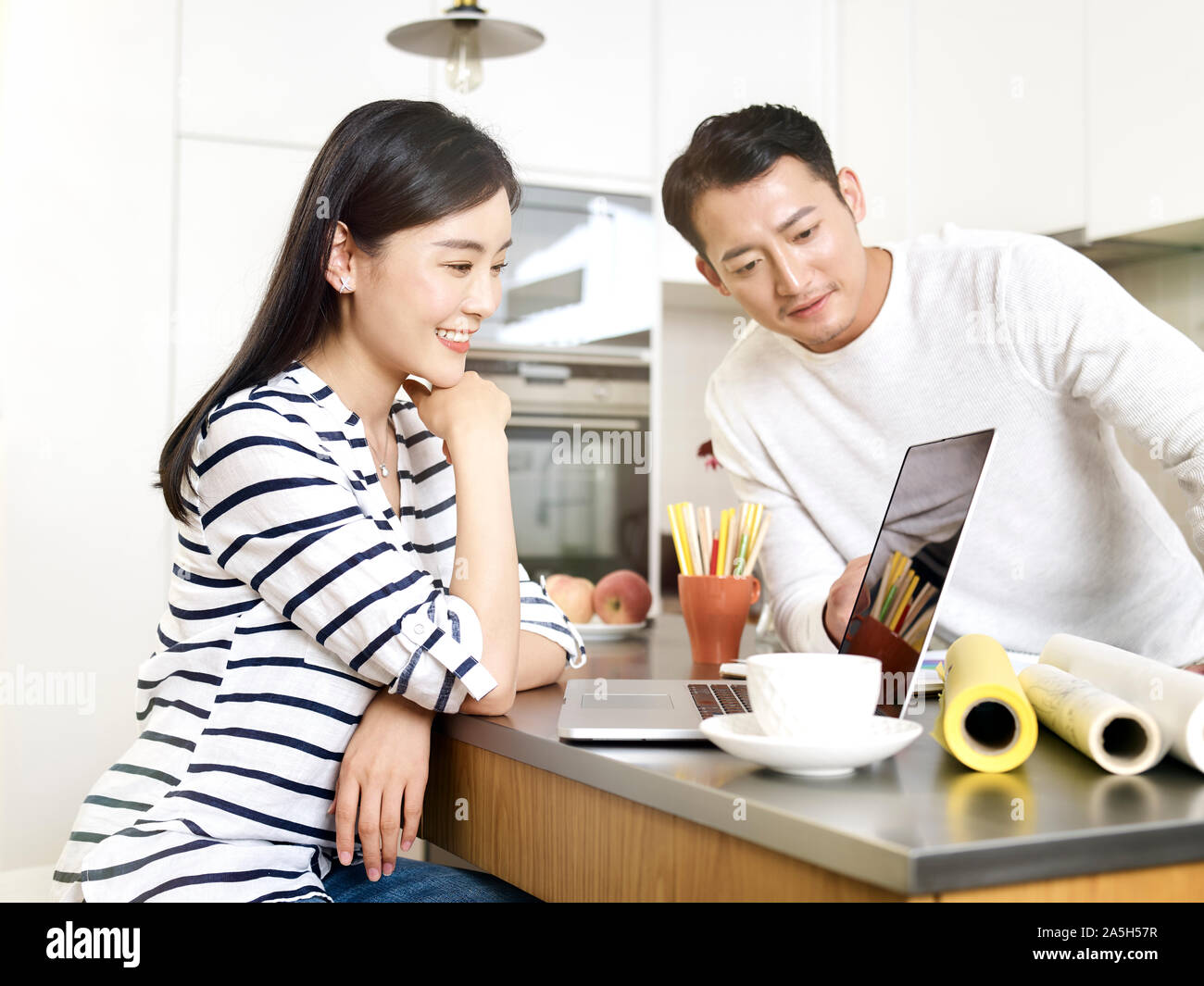 young asian couple freelance home workers using laptop computer in kitchen Stock Photo