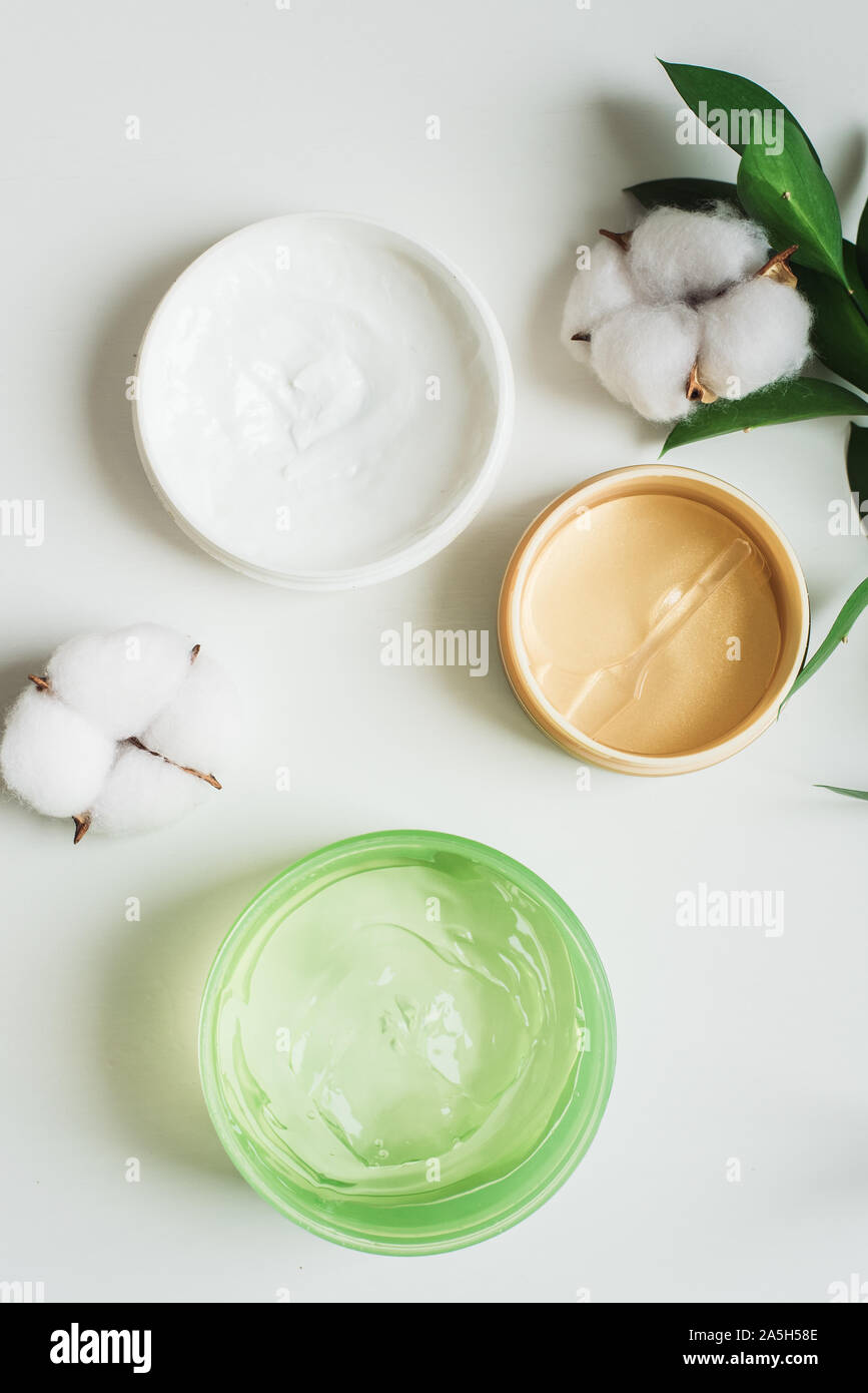 Jars of cream, aloe gel and moisturizing face patches on a white background next to cotton flowers. Nature Cosmetics for hand and face skin care, a means to reduce wrinkles on hands, moisturizing. Natural cosmetics from flower extract, beauty and fashion Stock Photo