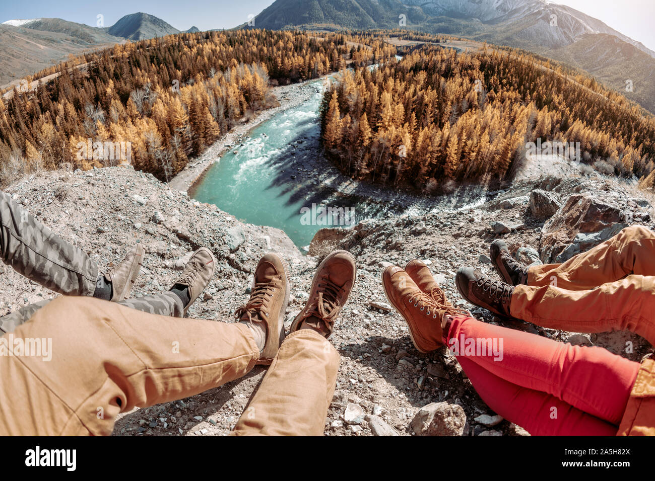 Four friends sits and looks on river and mountains. Close up photo of legs Stock Photo