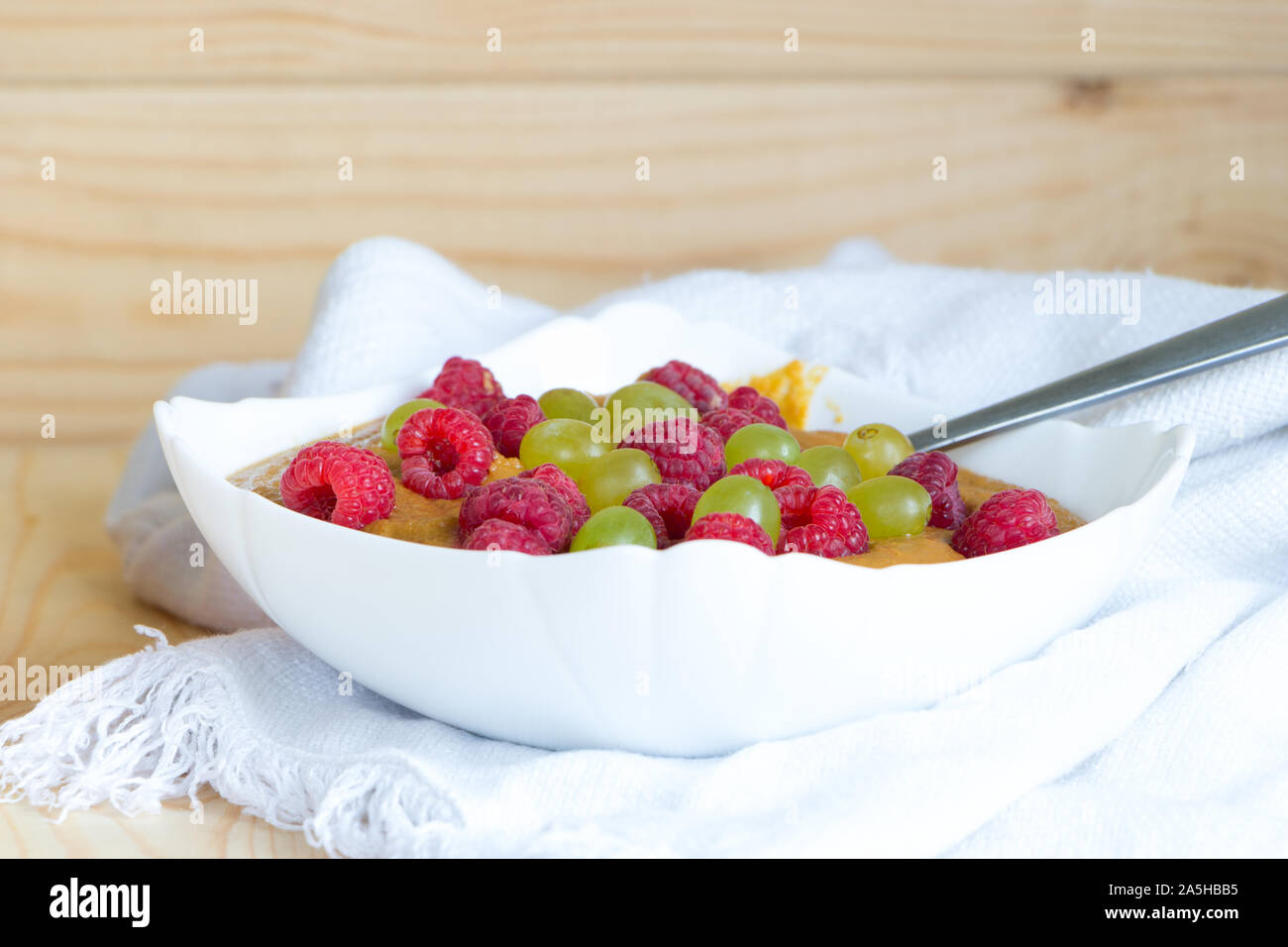 Delicious healthy raw food diet breakfast. Vegan flax porridge with raspberry and grape raisins in white bowl with spoon on linen fabric. Close-up Stock Photo
