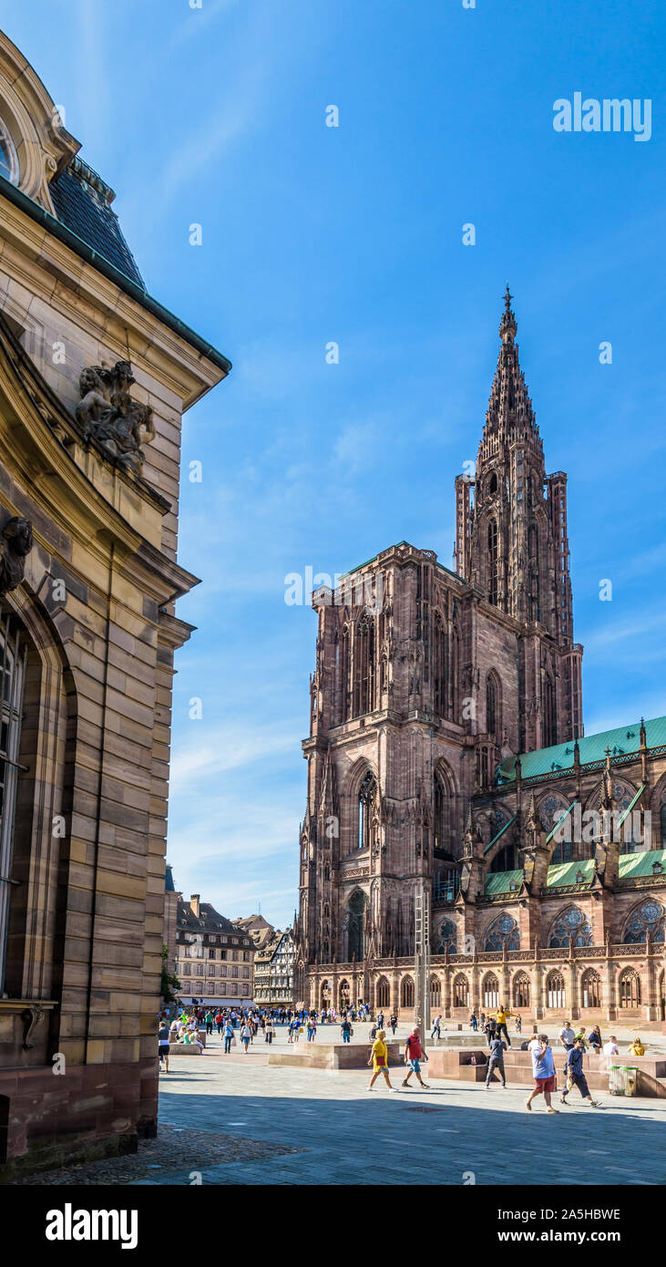 The spire of Notre-Dame cathedral in Strasbourg, France, with people strolling on the place du Chateau and the Rohan Palace on the foreground. Stock Photo