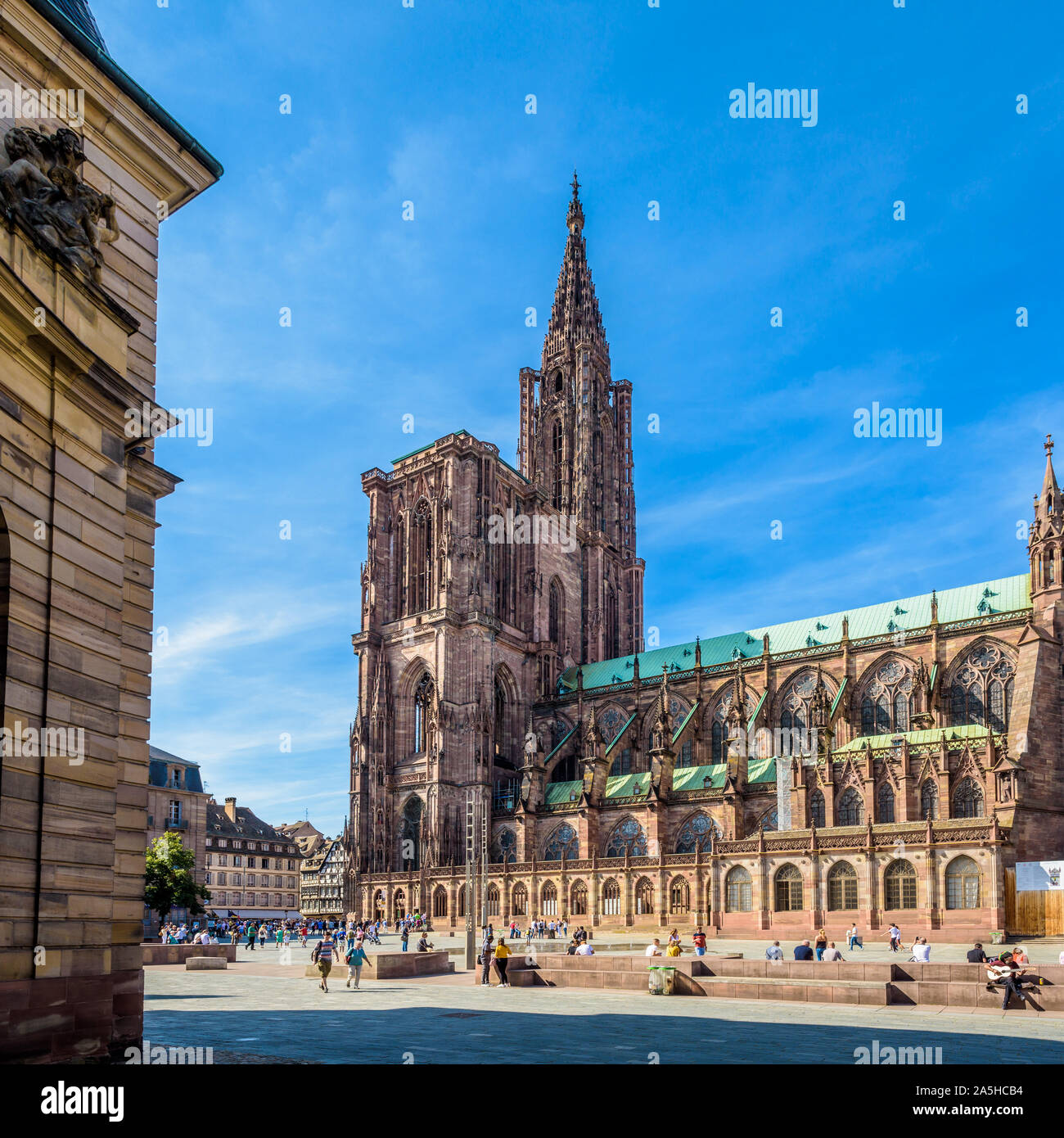 The spire of Notre-Dame cathedral in Strasbourg, France, with people strolling on the place du Chateau and the Rohan Palace on the foreground. Stock Photo