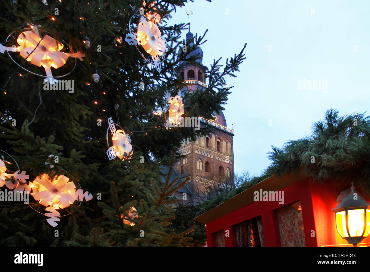 Christmas background with tree, festive warm yellow lights, lantern and church tower of Riga Dome Cathedral in Old Town, Latvia, New Year's Eve Stock Photo
